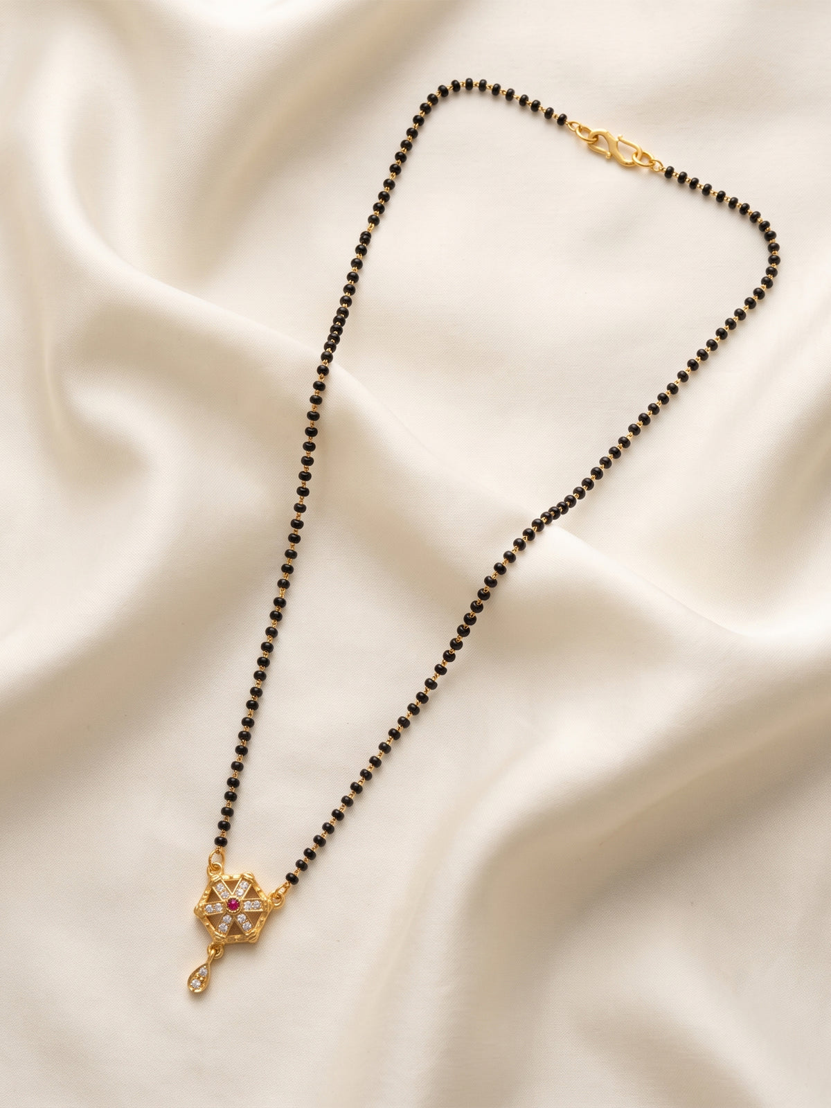 lfariya jewellery designer black bead mangalsutra necklace showcasing a luxurious gold plated square pendant with brilliant gemstone detailing, beautifully styled on a decorative white plate with floral accents.