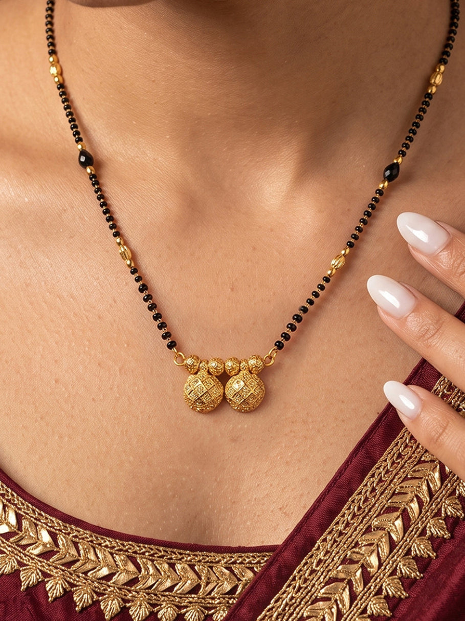 A close-up of a woman wearing a traditional Indian black beaded necklace with gold-toned decorative beads and a double spherical pendant, paired with a maroon embroidered blouse.