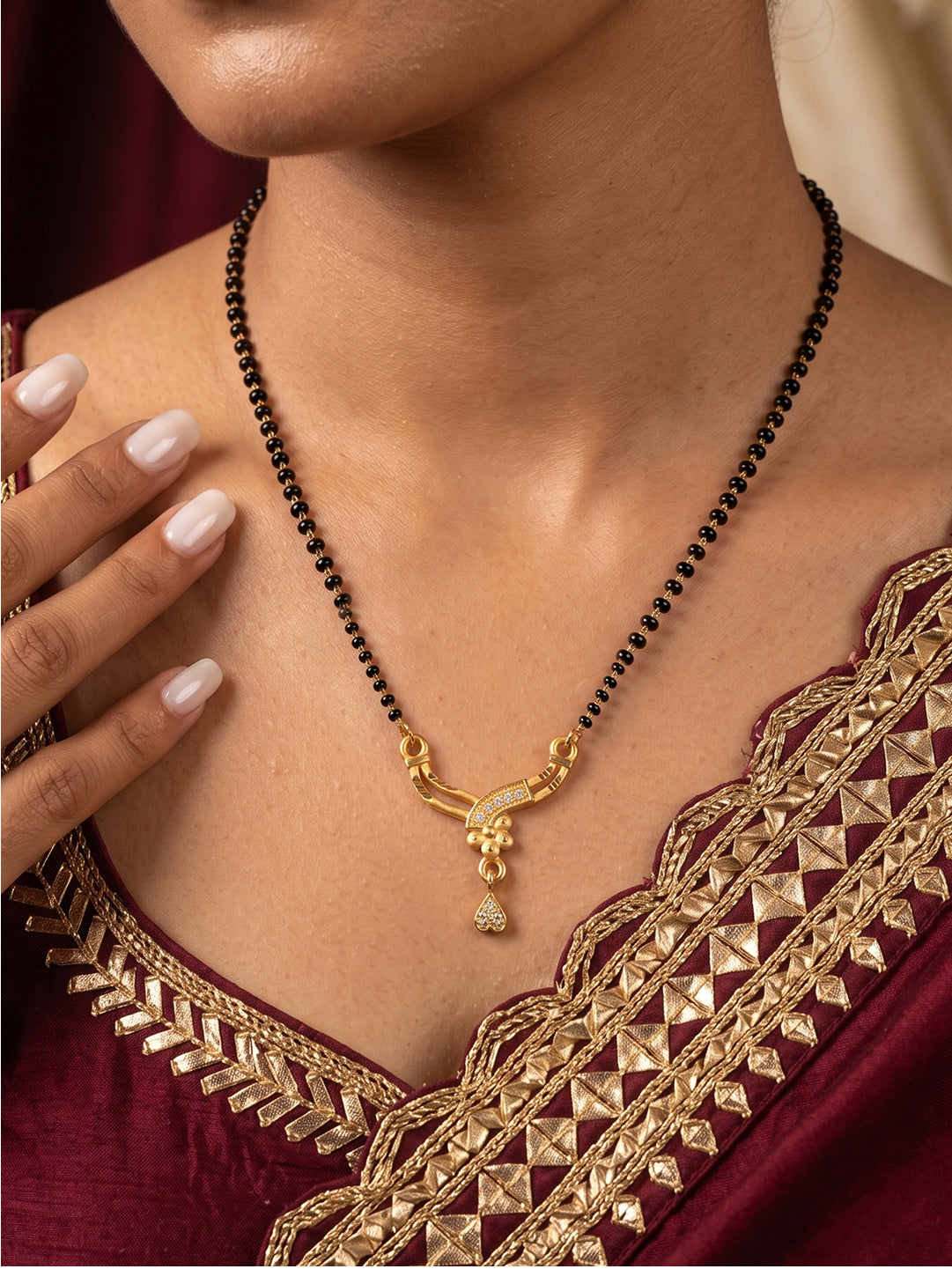 Traditional curved drop mangalsutra with black beads chain, CZ-studded gold pendant and heart-shaped drop by Lfariya Jewellery.