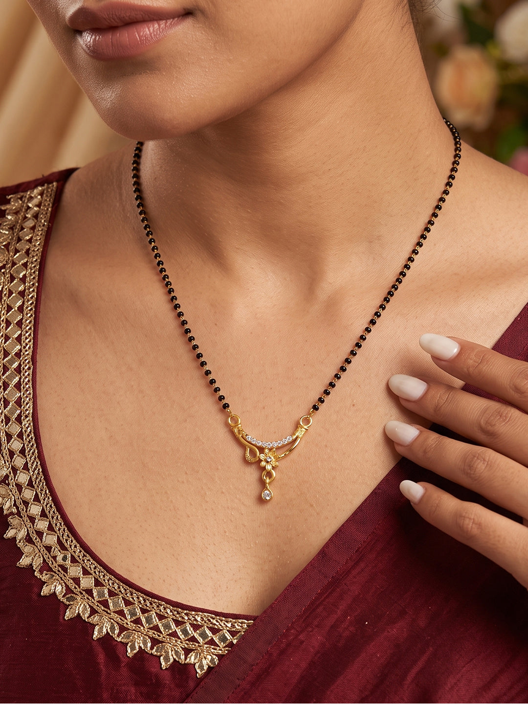 Traditional black bead mangalsutra featuring a curved gold-tone floral pendant with sparkling CZ stones and a dangling drop by Lfariya Jewellery.