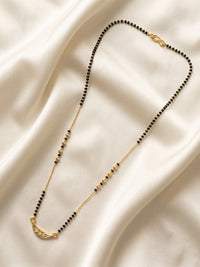 A delicate gold-tone necklace with small black beads and a crescent moon pendant set with tiny clear stones, displayed on draped cream satin fabric lfariya jewellery.