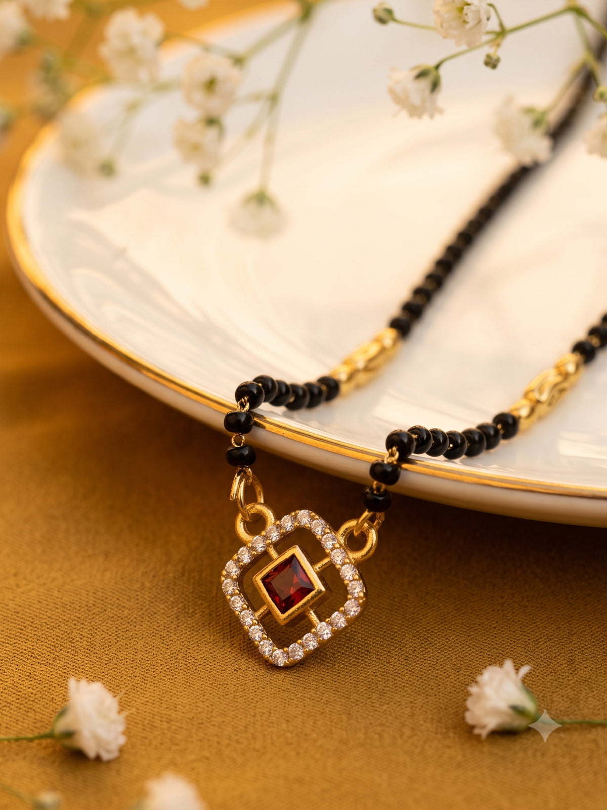 lfariya jewellery gold and black beaded mangalsutra necklace with a square American Diamond pendant featuring a red center stone, displayed on a white ceramic plate with gold trim and delicate white flowers.